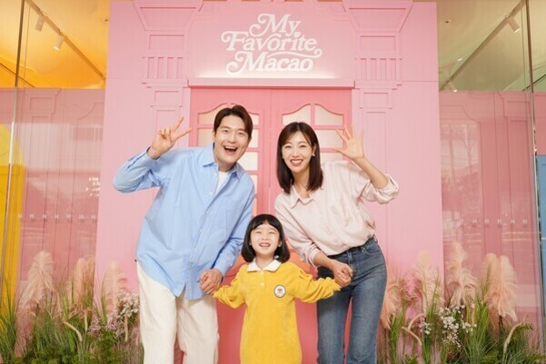 분홍색 배경 앞에서 가족 세 명이 손을 잡고 밝게 미소 지으며 포즈를 취하고 있다. 뒤에는 'My Favorite Macao'라는 글씨가 보인다.