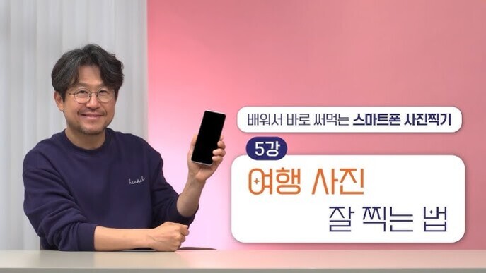안경을 쓴 남성이 테이블에 앉아 스마트폰을 들고 미소짓고 있다. 옆에는 '배워서 바로 써먹는 스마트폰 사진찍기', '5강 여행 사진 잘 찍는 법'이라는 문구가 적혀있다.