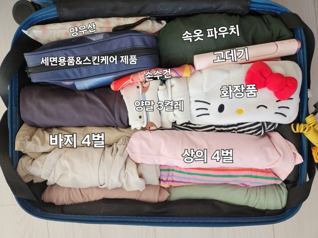 여행용 가방 안에 양우산, 세면용품&스킨케어 제품, 속옷 파우치, 고데기, 손수건, 양말 3켤레, 화장품 파우치, 바지 4벌, 상의 4벌이 정리되어 담겨 있다.