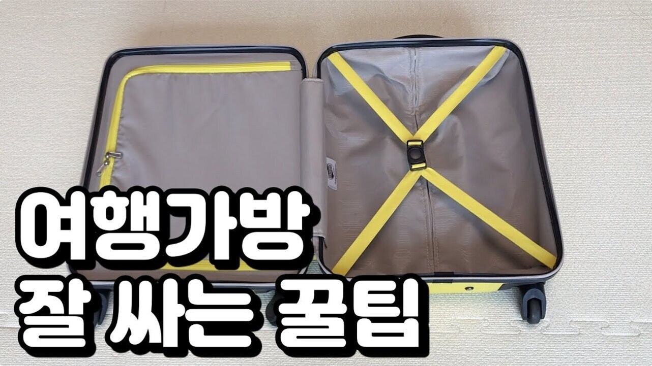 빈 여행가방이 바닥에 펼쳐져 있고, 가방 내부는 노란색 지퍼와 고정밴드로 구성되어 있다. 왼쪽 하단에는 '여행가방 잘 싸는 꿀팁'이라는 한글 문구가 크게 적혀 있다.
